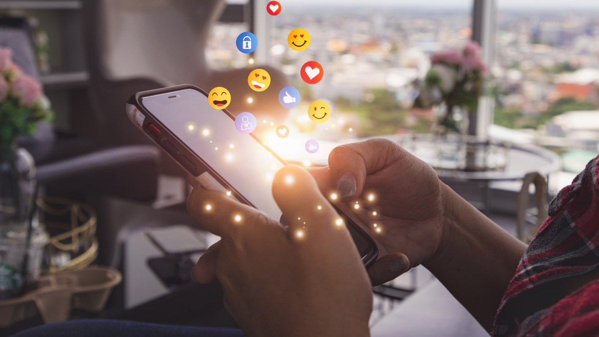 Nahaufnahme Smartphone in der Hand, Emojis springen aus Screen hervor.