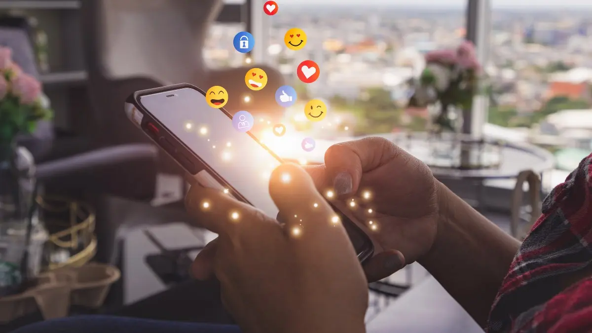 Nahaufnahme Smartphone in der Hand, Emojis springen aus Screen hervor.